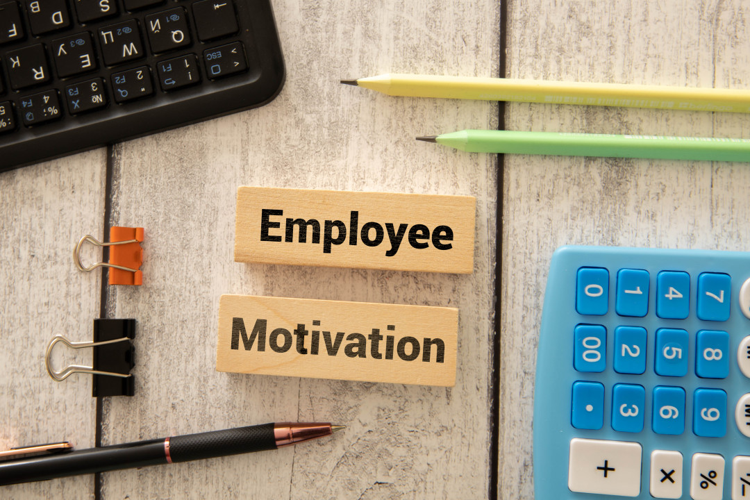 EMPLOYEE MOTIVATION text on the business card written in blue pencil near the keyboard on a blue background